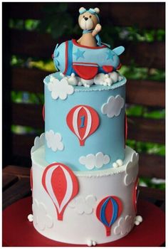 a blue and white cake with a teddy bear on top is sitting on a red table