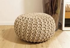 a round woven ottoman sitting on top of a hard wood floor next to a potted plant