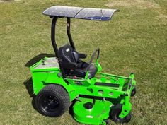 a green lawn mower sitting on top of a lush green field next to a solar panel