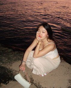 a woman sitting on the beach with her hand in her mouth