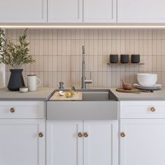 a kitchen with white cupboards and countertops has a sink, dishwasher, coffee maker and cups on it