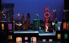 performers perform on stage in front of the city skyline with neon signs and buildings behind them