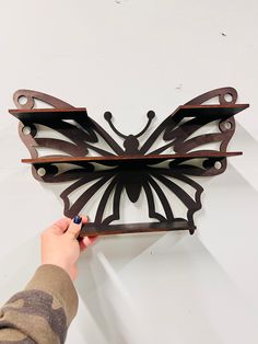 a person is holding a metal butterfly on a shelf with two shelves above it and the bottom half of the wall behind them