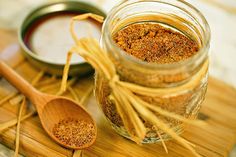 a jar filled with spices sitting on top of a wooden table next to two spoons