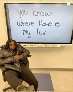 a woman sitting on a chair in front of a large screen with writing on it