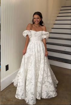 a woman in a white dress standing next to stairs and smiling at the camera with her hands on her hips