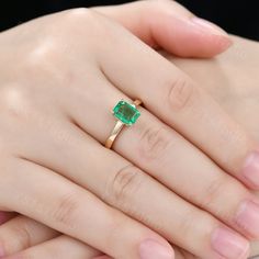 a woman's hand holding an emerald ring