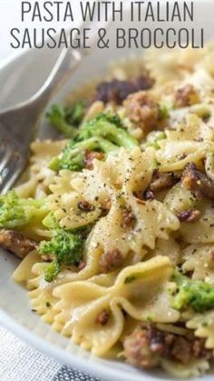 pasta with sausage and broccoli in a white bowl next to a fork on a table