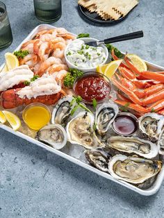 an assortment of seafood on a platter with dipping sauces and lemon wedges