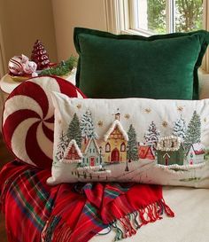 two christmas pillows sitting on top of a couch next to a pillow with a village scene