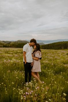 an engaged couple kissing in a field with wildflowers