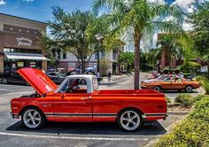 an old red truck with its hood open parked in front of a building and palm trees