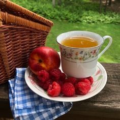 a cup of tea and some raspberries sit on a plate next to a basket