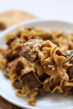 a white plate topped with pasta and meat covered in sauce on top of a wooden table