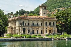 a large building sitting on top of a lake next to a lush green forest covered hillside