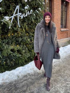 a woman is standing in front of a christmas tree wearing a gray dress and fur coat