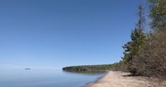 a sandy beach next to the ocean with trees on both sides and blue sky above