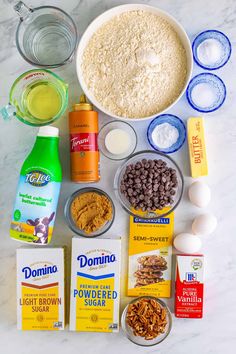 ingredients to make chocolate chip cookies laid out on a marble counter top, including eggs, milk, flour, and other items