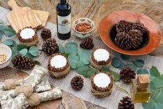 pine cones and candles are sitting on a table next to some leaves, nuts, and a bottle of wine