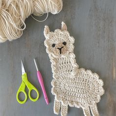 a crocheted llama next to scissors and yarn on a gray surface with two skeins