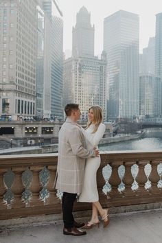 a man and woman standing next to each other on a bridge in front of tall buildings