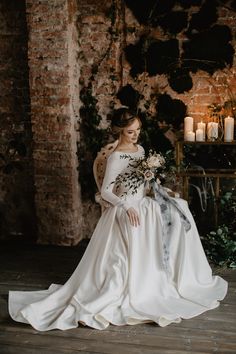 a woman in a white wedding dress holding a bouquet and sitting on a chair next to a brick wall