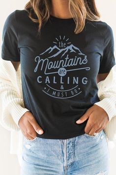 Introducing our "The Mountains Calling And I Must Go" Graphic Tee, a perfect choice for adventure enthusiasts and outdoor lovers. Most t shirt colors are 52/48 cotton/poly blend. White and Cream tees are 100% cotton, Ash tees are 99/1 cotton/poly. Available in various sizes, it's an excellent addition to outdoor retail stores and adventure-themed boutiques. Encourage your customers to answer the call of the mountains with our "The Mountains Calling And I Must Go" Graphic Tee. By Kissed Apparel.M Outdoor Crew Neck T-shirt With Letter Print, Black T-shirt With Letter Print For Outdoor, Cotton Graphic Print Tops For Outdoor Activities, Casual Slogan T-shirt For Outdoor, Blue Outdoor Tops With Screen Print, Blue Graphic Tee For Outdoor Activities, Blue Tops With Screen Print For Outdoor Activities, Blue Screen Print Tops For Outdoor Activities, Crew Neck T-shirt With Letter Print For Outdoor