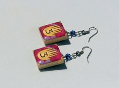 You probably can't check these for information on Gravity Falls, but wearing them will still make you the envy of all who venture into the Mystery Shack!  These earrings are made from 'upcycled' Scrabble tiles and feature artwork inspired by the show 'Gravity Falls', with purple beads accenting the color of the journal. Gravity Falls Jewelry, Gravity Falls Earrings, Funky Earrings Aesthetic, Silly Earrings, The Mystery Shack, Lesbian Earrings, Crazy Earrings, Weird Earrings, Creative Earrings