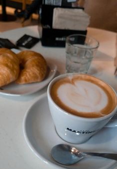 there is a cup of coffee and two croissants on the plate next to each other