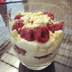 a dessert with raspberries and whipped cream in a glass bowl on a table