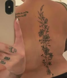 a woman with tattoos on her back holding a cell phone