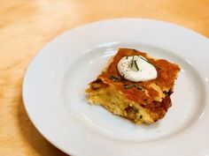 a piece of food on a white plate sitting on a wooden table with a fork