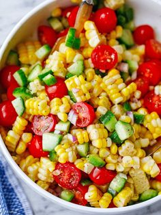 a white bowl filled with corn, tomatoes and cucumber on top of a blue towel