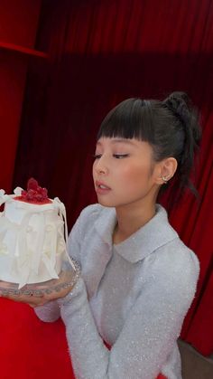 a woman holding a cake with white frosting and strawberries on it, in front of a red curtain