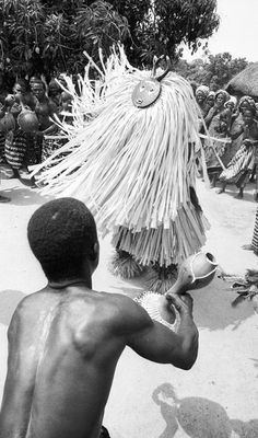 a group of people standing around each other in front of some grass huts and trees