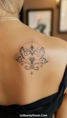 the back of a woman's shoulder with an ornamental tattoo design on her left shoulder