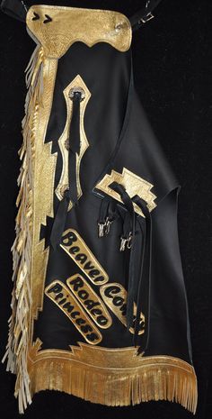 "Custom Chaps, handmade in the U.S.A.! These chaps are made with a quality, black chap leather. They have metallic gold, chap leather trim pieces on them. They have 6\" metallic gold fringe on the leg and there are three metal conchos and two chap snaps on each leg as well. We will also stitch custom lettering on both sides, making these an excellent choice for rodeo royalty! Price is $3 per letter.  Please message us for measurements when you order.  Thanks for looking! Note: We do custom work as well so If you need specific measurements or have something special in mind feel free to contact us. Our phone # is (406) 426-4300. We also have a variety of chinks, chaps and kid's chinks that are in stock now and ready for shipment. So if you're in a hurry feel free to contact us to see what we Custom Chaps, Rodeo Chaps, Gold Fringe, Custom Letters, Custom Leather, Leather Trim, Metallic Gold, Farm Animals, Rodeo