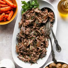 a white plate topped with meat and carrots next to bowls of baby carrots