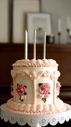 a white cake with pink flowers and candles sitting on top of a doily plate