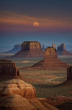 the full moon is setting over monument buttes