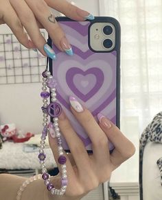 two hands holding an iphone case with purple hearts on it and beads hanging from the back