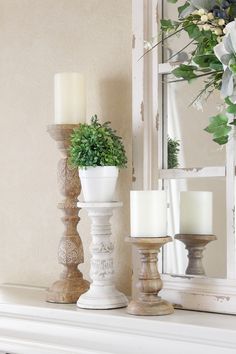 three candles are sitting on a mantle with flowers and greenery in front of the mirror