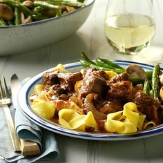 a white plate topped with pasta and meat covered in gravy next to green beans