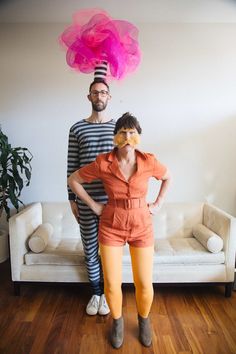 a man and woman standing next to each other in front of a couch with a pink hat on their head