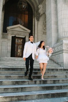 a man and woman are walking down the stairs in front of a building with flowers