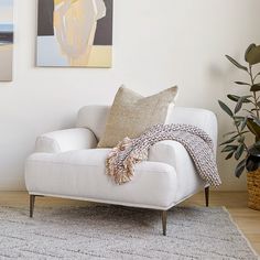 a white chair sitting in front of a painting on the wall next to a potted plant