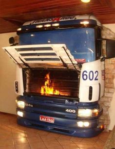 a large blue truck parked in front of a brick wall with a pizza oven on it's side