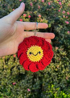 a hand holding a crocheted red flower with a smiley face on it's center