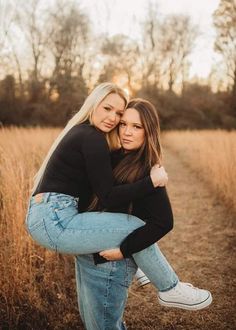 two women hugging each other in the middle of a field with tall grass and trees