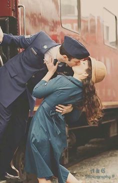 a man and woman kissing in front of a train